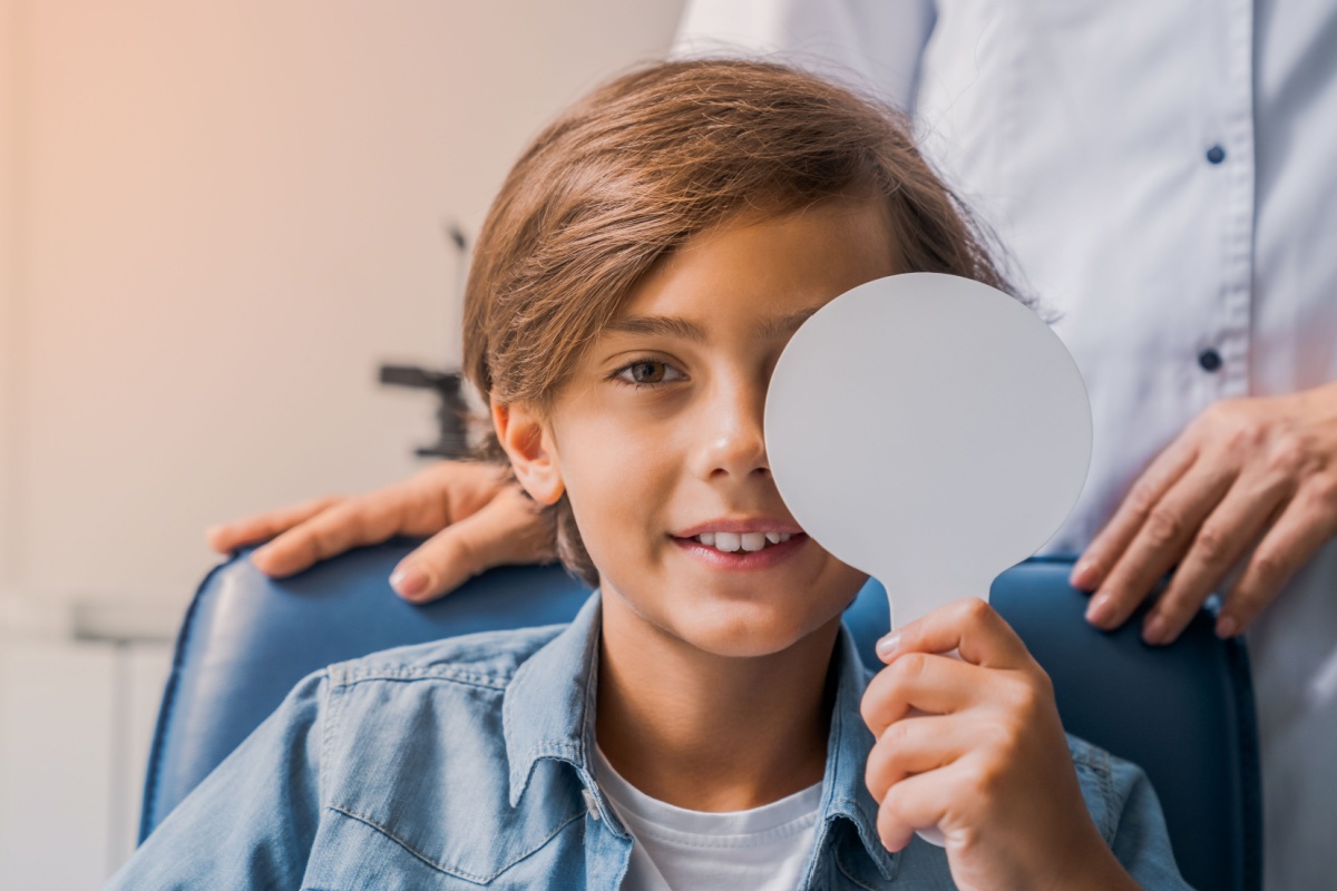 Boy holding occluder over his left eye during an eye exam.